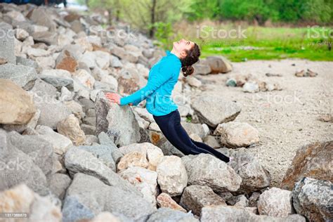 Cheerful Teenage Girl Stretching Against Rock Embankment Bending Over