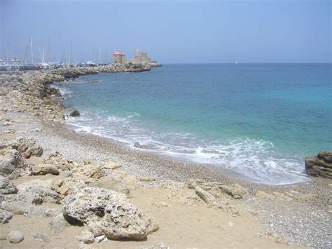 The Beach Is Rocky And Blue With Boats In The Water