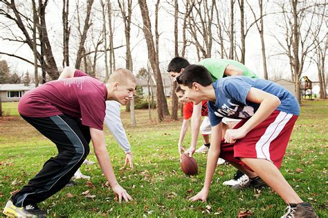 Smiling Friends Playing American Football While Bending Over Field In