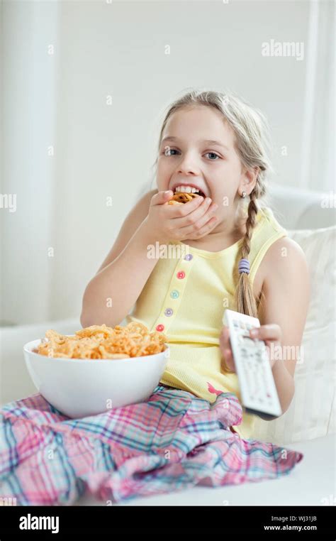 Girl Watching Tv As She Stuffs Her Mouth With Wheel Shape Snack Pellets