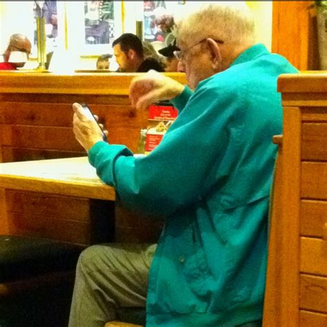 An Old Man Sitting At A Table Using His Cell Phone