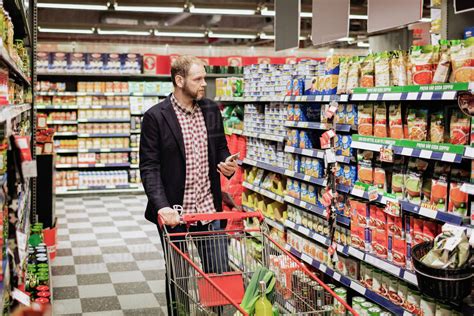 Man Using Smart Phone While Shopping In Grocery Store Stock Photo