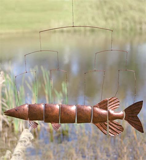 A Metal Fish Sculpture Hanging From A Wire Next To A Body Of Water With