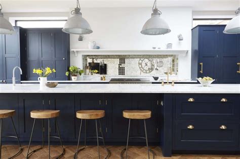 Beautifully appointed blue and white kitchen boasts navy blue cabinets fitted with polished nickel hardware and a white quartz countertop positioned beneath white folding windows and wrapping around to a stainless steel oven range placed against white beveled subway backsplash tiles beneath white upper cabinets. Dark Kitchen and Metals Combination Images | Kitchen Magazine