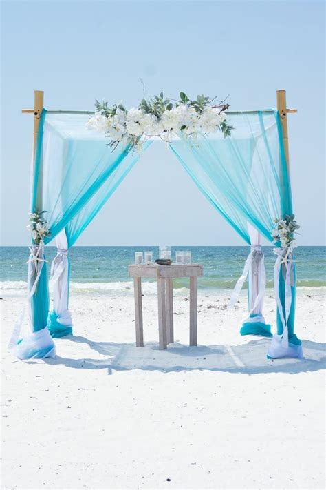 An Outdoor Wedding Setup On The Beach With Blue Drapes And White