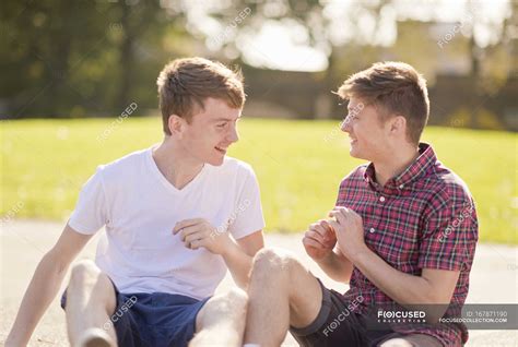 Two Young Male Friends Chatting In Park — Three Quarter Length