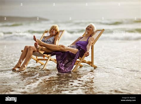Two Happy Mature Women Relaxing In Deck Chairs On The Beach Stock Photo