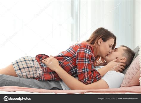 Cute young loving couple kissing while lying on bed at home — Stock Photo © belchonock #207300060