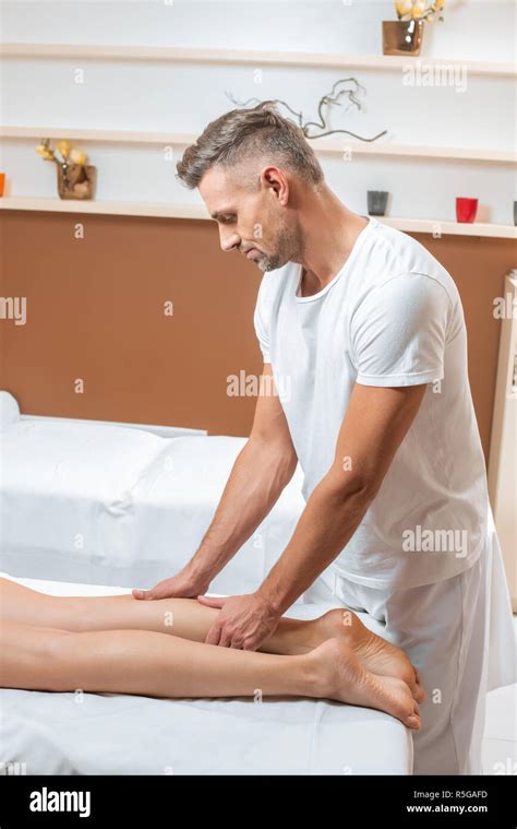 Handsome Man Massaging Woman Legs On White Massage Table Stock Photo