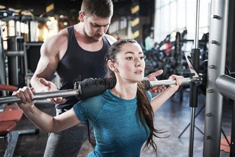 Personal Trainer Man Helps Woman Work With Barbell At Squat Exercises