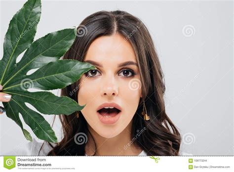 beauty portrait of an excited woman with short brunette hair posing with green leaf over white