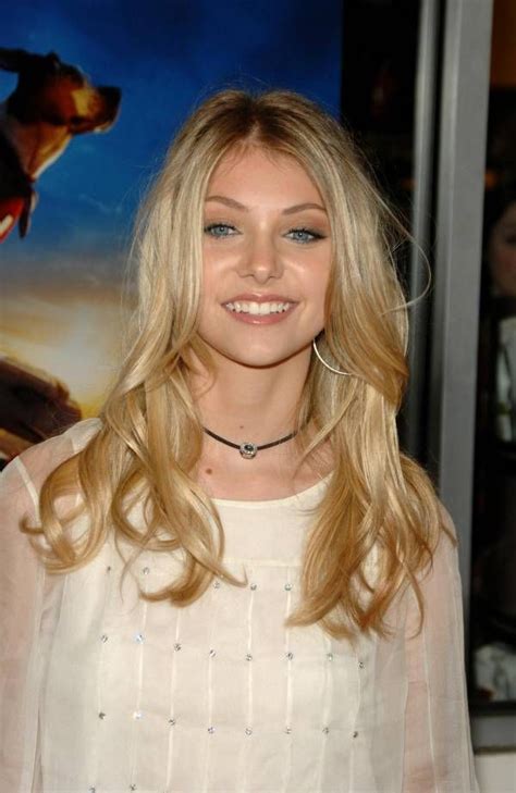 A Woman With Long Blonde Hair Smiling At The Camera And Wearing A White