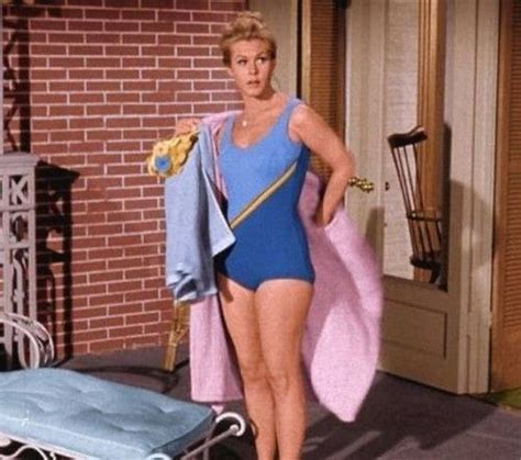 A Woman In A Blue Swimsuit Standing Next To A Bed With A Towel On It