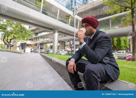 Indian Businessman Sitting Outdoors In City While Having Coffee Break