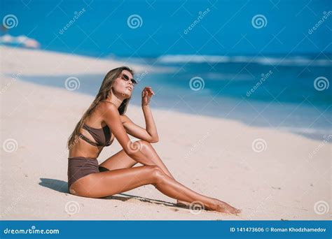 Beautiful Tanned Girl Posing On Beach With White Sand And Blue Ocean