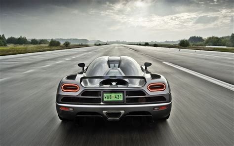 A Black Sports Car Driving Down The Road With Dark Clouds In The Sky