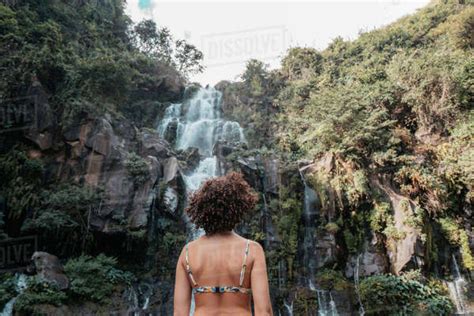 Rear View Of Woman In Bikini Standing Against Waterfall At Forest
