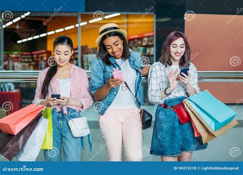 Young Women With Shopping Bags Using Smartphones Young Girls Shopping