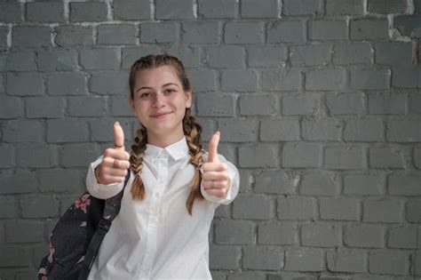 Premium Photo Young Beautiful Schoolgirl Shows Like On Gray Brick Wall Background