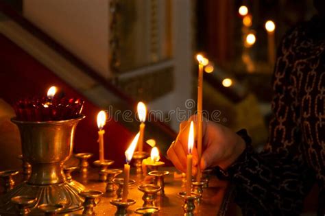 Hand With A Lit Candle In The Church A Woman Puts A Candle To Her Saint