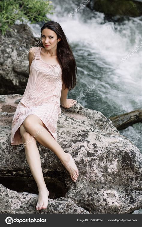 Beautiful Brunette Sitting On A Rock In The Middle Of The River Water
