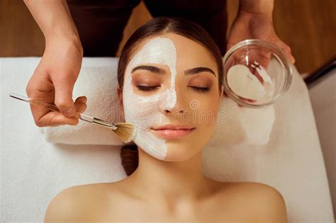 On Face Of Woman Beautician Applies A Mask In The Spa Salon Stock Photo