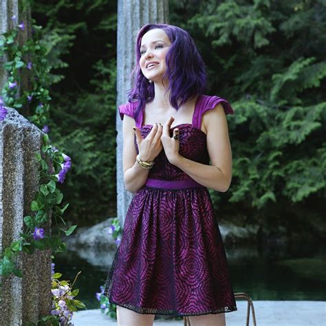 A Woman With Purple Hair Is Standing In Front Of Some Trees And Flowers Holding Her Hands Together