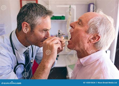 Male Doctor Checking Senior Male Patient Mouth With Otoscope Stock