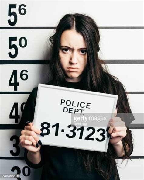 A Young Woman Standing In Front Of A Mugshot Wall In A Police Station