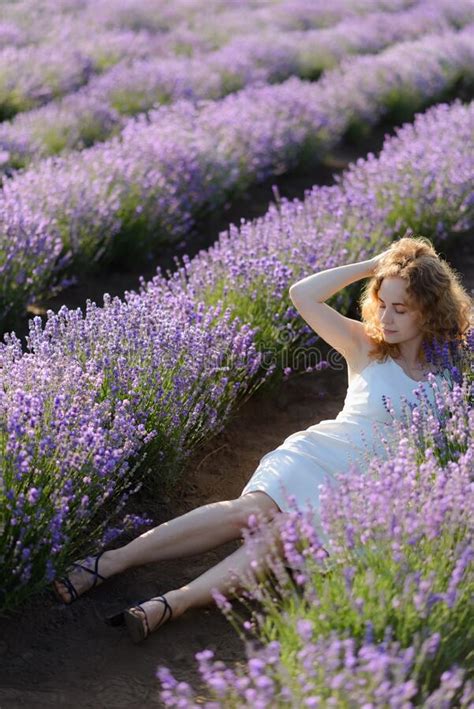 Young Caucasian Beautiful Woman In A White Dress Smelling Flowers In A Lavender Field Stock