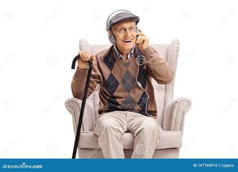 Elderly Man Sitting In An Armchair And Listening To Music On Earphones