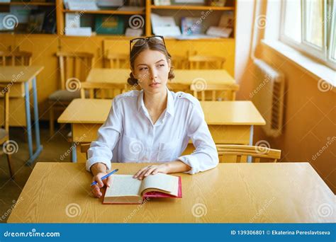 A Young Woman Sitting At A Desk In A White Shirt A Book On The Table