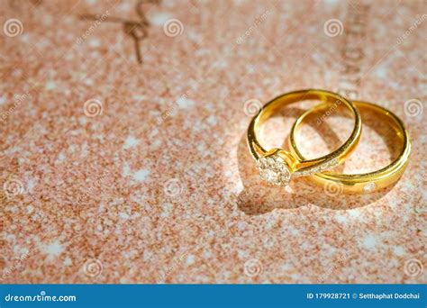 Close Up Of Gold Wedding Rings Or Engagement Rings On Wedding Invitation Card Background Stock