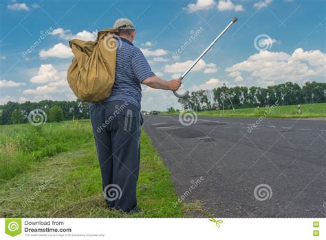 Man With Sack Standing On A Roadside Holding Walking Stick Up Stock