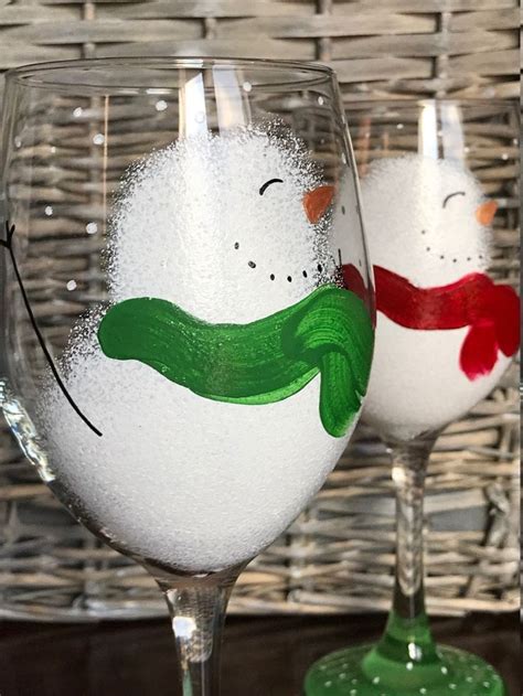 Two Wine Glasses With Snowmen Painted On Them Sitting In Front Of A Wicker Basket