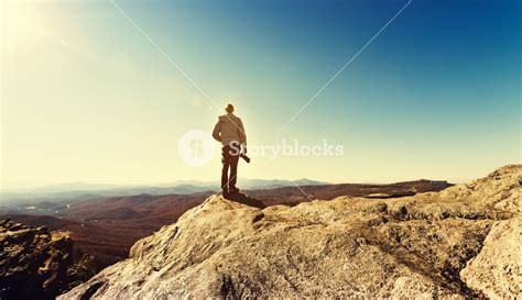 Man With A Camera Standing At The Edge Of A Cliff Overlooking The