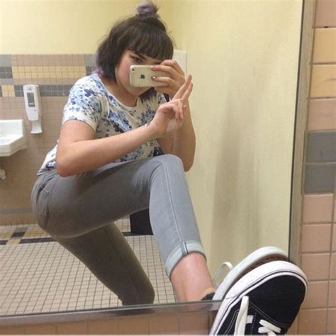 A Woman Taking A Selfie In A Bathroom Mirror With Her Cell Phone Up To