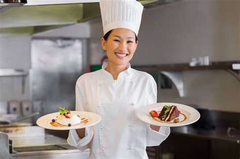 Confident Smiling Female Chef Holding Two Plates Cooked Food In Kitchen