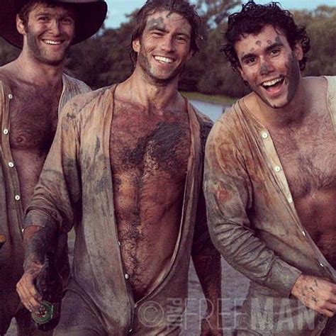 three men with mud on their bodies and one holding a bottle in his hand while standing next to
