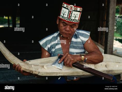 Aboriginal Man Wearing A Traditional Hat Carving Wood In A Village On