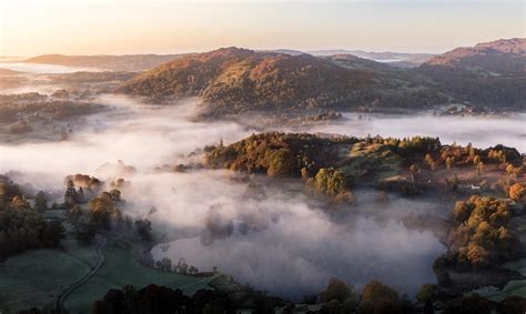 Autumn Mist Burns Off As The Sun Rises Over Loughrigg Tarn In The Lake