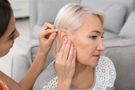 Young Woman Putting Hearing Aid In Mothers Ear Indoors Able Hearing