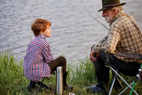 Grandfather And Grandson Fishing On River Berth Elderly Man Talking To