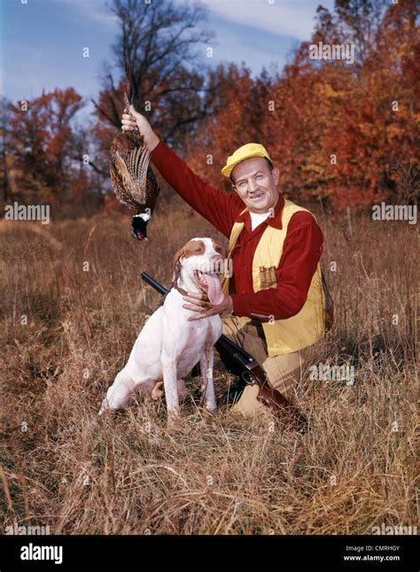 1950s 1960s Man Hunter With Shotgun Holding Up Bird Pheasant Kneeling