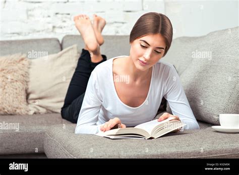 belle jeune femme allongée sur le canapé en lisant un livre dans la salle de séjour à la maison