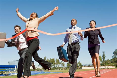 Woman Crossing The Finish Line With Colleagues Running Stock Photo