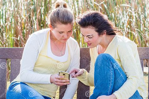 Two Happy Friends Sitting On Park Bench Talking And Interacting Stock