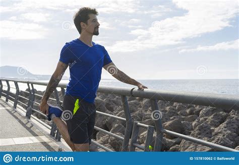 Fitness Runner Smiling While Stretching His Leg In A Fence In Front Of