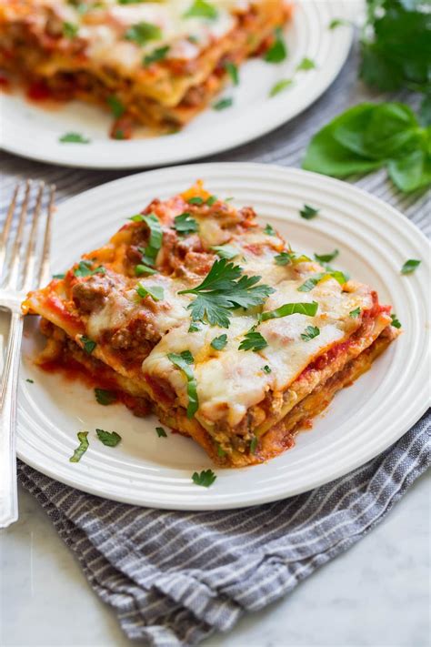 two white plates topped with lasagna covered in cheese and sauce next to a fork
