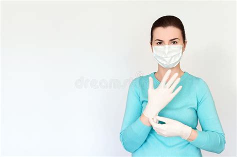 Woman In Medical Mask Puts On Rubber Surgical Gloves Shot On A Light